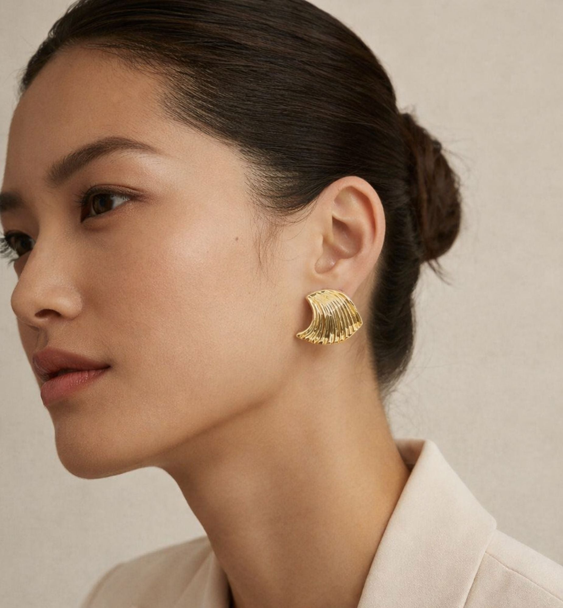 Woman wearing gold earrings with a neutral background