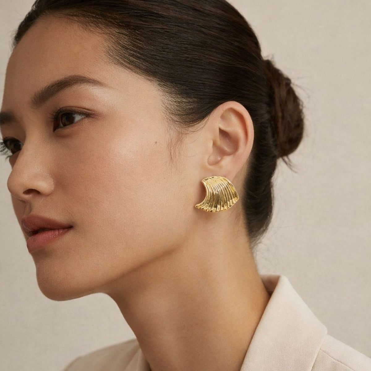 Woman wearing gold earrings with a neutral background