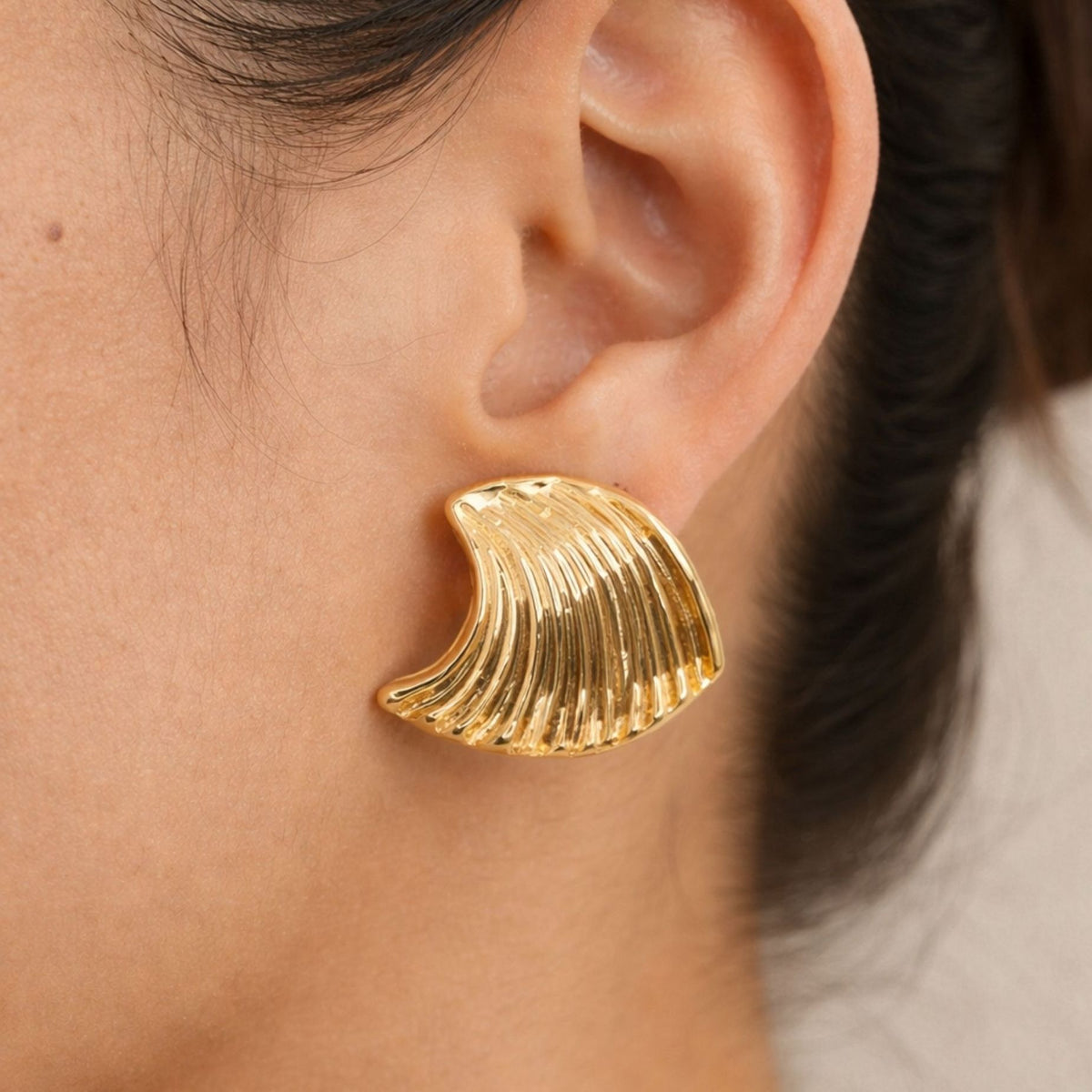 Gold leaf-shaped earring worn by a person