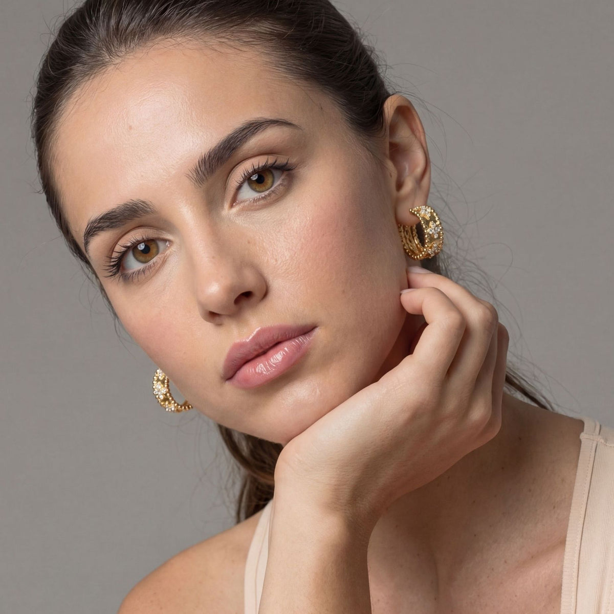 Woman wearing gold earrings against a neutral background